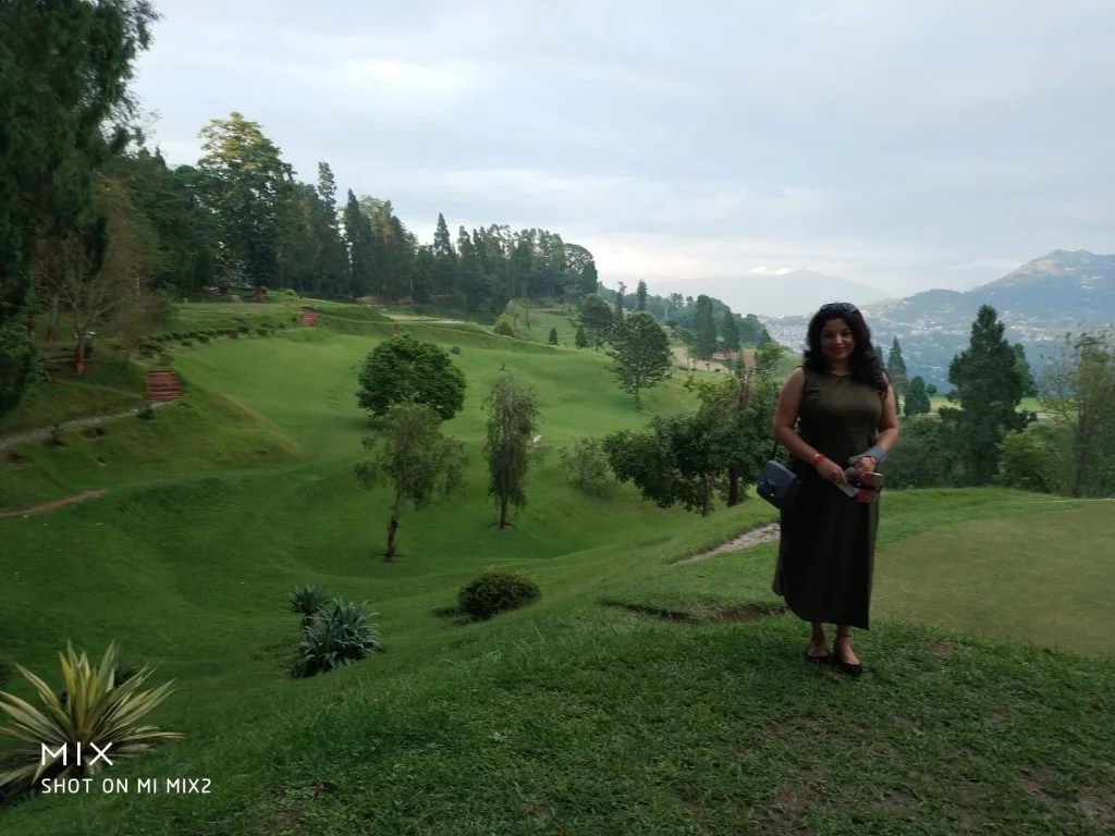 A woman standing at a scenic 9-hole golf course in Kalimpong