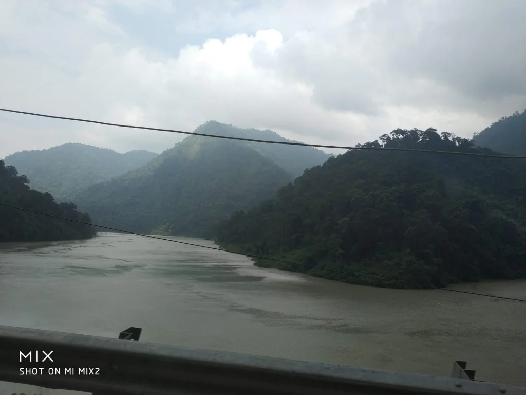 A wide view of the Teesta River flowing through lush green hills under a cloudy sky